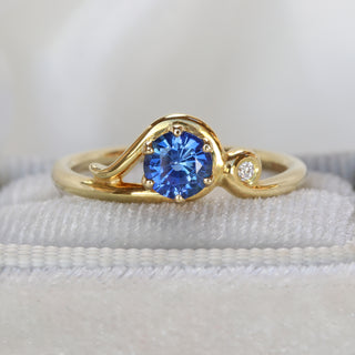 18ct gold Art Nouveau sapphire engagement ring on soft fabric cushion.
