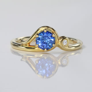 Handmade 18ct gold Art Nouveau sapphire engagement ring with Canadian diamond on reflective surface.
