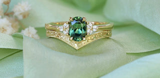 18ct gold green sapphire and diamond cluster engagement ring with orange blossom engraved wishbone wedding band, resting on green ribbon