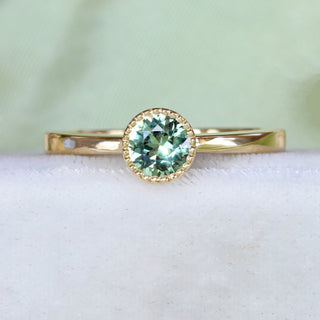 Handmade 18ct gold green sapphire solitaire engagement ring on pale textured fabric.