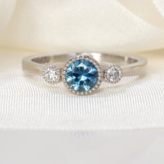 Front profile of handmade platinum trilogy engagement ring with teal sapphire and Canadian diamonds.