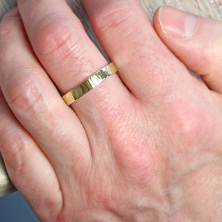 A gold treebark texture ring shown on  a male finger