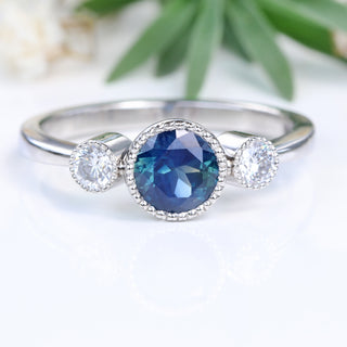 Platinum trilogy engagement ring with Parti sapphire photographed against greenery.