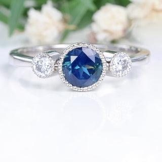 PArti sapphire trilogy engagement ring on white background with floral backdrop.