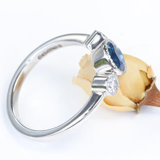 Platinum diamond and Parti sapphire trilogy ring shown at an angle, resting on yellow rose.