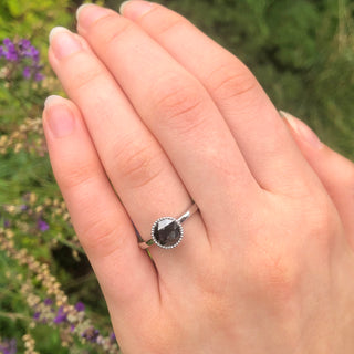 Platinum black diamond ring with rose cut centre gemstone shown on hand in natural light.