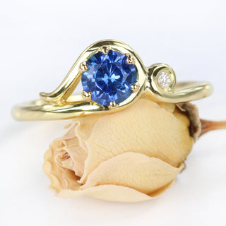 Ceylon sapphire Art Nouveau inspired engagement ring resting on a rose flower.