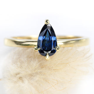 Close up of deep blue sapphire solitaire engagement ring on seed head.