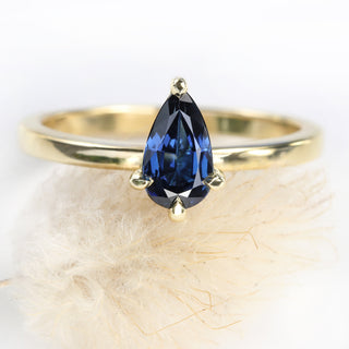 Pear cut sapphire 18ct gold engagement ring resting on a seed head.