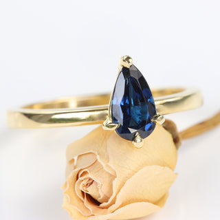 Teardrop sapphire engagement ring with deep blue gemstone shown at an angle.
