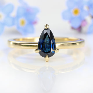 Pear cut blue sapphire solitaire engagement ring with blue flowers.