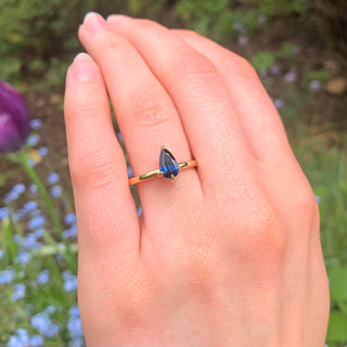 Ethical engagement ring with pear cut deep blue sapphire worn outdoors.