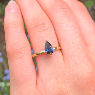 Deep blue teardrop sapphire engagement ring in 18ct gold worn on hand.