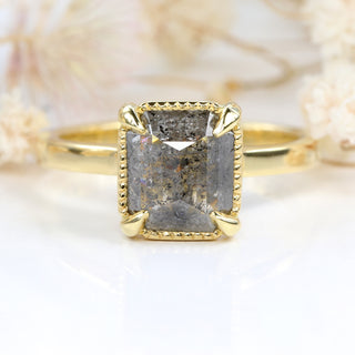 18ct gold emerald cut salt and pepper diamond ring photographed on pale floral background
