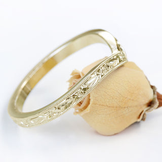 A gold wishbone ring with textured pattern, shown from the side view balanced on a flower