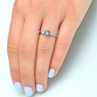 Platinum Sapphire trilogy engagement ring on the hand, with pale blue backdrop.