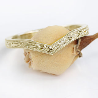A gold wishbone ring with textured pattern balanced on a flower