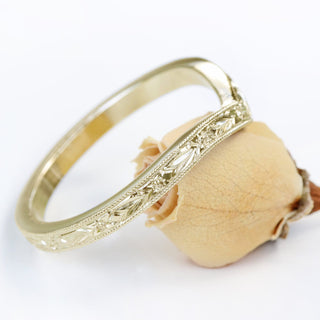 A gold wishbone ring with textured pattern, shown from the side view balanced on a flower