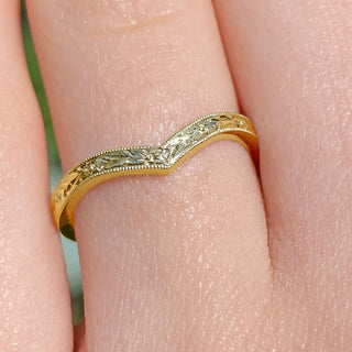A gold textured wishbone ring shown close up on a finger