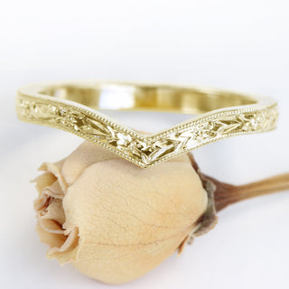 A gold wishbone wedding ring with an engraved orange blossom pattern on a white background.