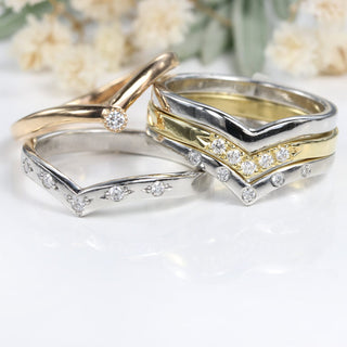 A stack of Lilia Nash wishbone or curved wedding bands, some set with diamonds