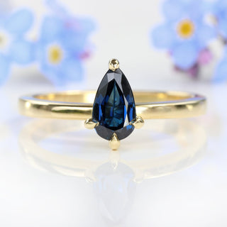 Pear cut blue sapphire solitaire engagement ring with blue flowers.