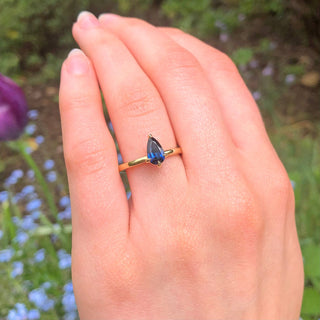 Ethical engagement ring with pear cut deep blue sapphire worn outdoors.