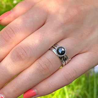 Black diamond solitaire engagement ring and matching wedding band, shown worn against greenery.