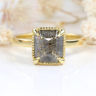 18ct gold emerald cut salt and pepper diamond ring photographed on pale floral background
