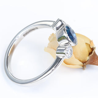 Platinum diamond and Parti sapphire trilogy ring shown at an angle, resting on yellow rose.