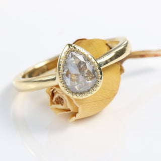Pear cut salt and pepper diamond solitaire ring on orange rose bud