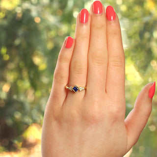 Princess cut sapphire and diamond cluster ring photographed outdoors on greenery.