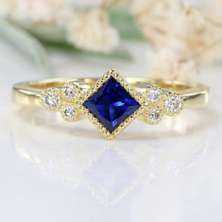 18ct gold princess cut sapphire ring photographed on white floral background.