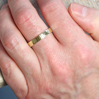 A gold treebark texture ring shown on  a male finger