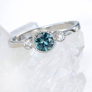 Platinum trilogy engagement ring with teal Montana sapphire and diamonds photographed on crystal surface.