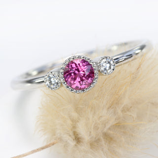 Close-up of pink sapphire and diamond trilogy ring on seed head
