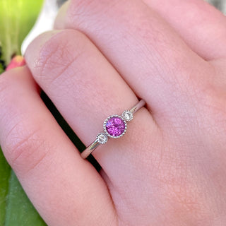 Platinum pink sapphire trilogy engagement ring worn on hand outdoors.