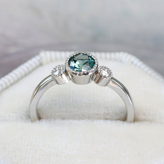 Platinum teal sapphire trilogy engagement ring presented in white ring box.